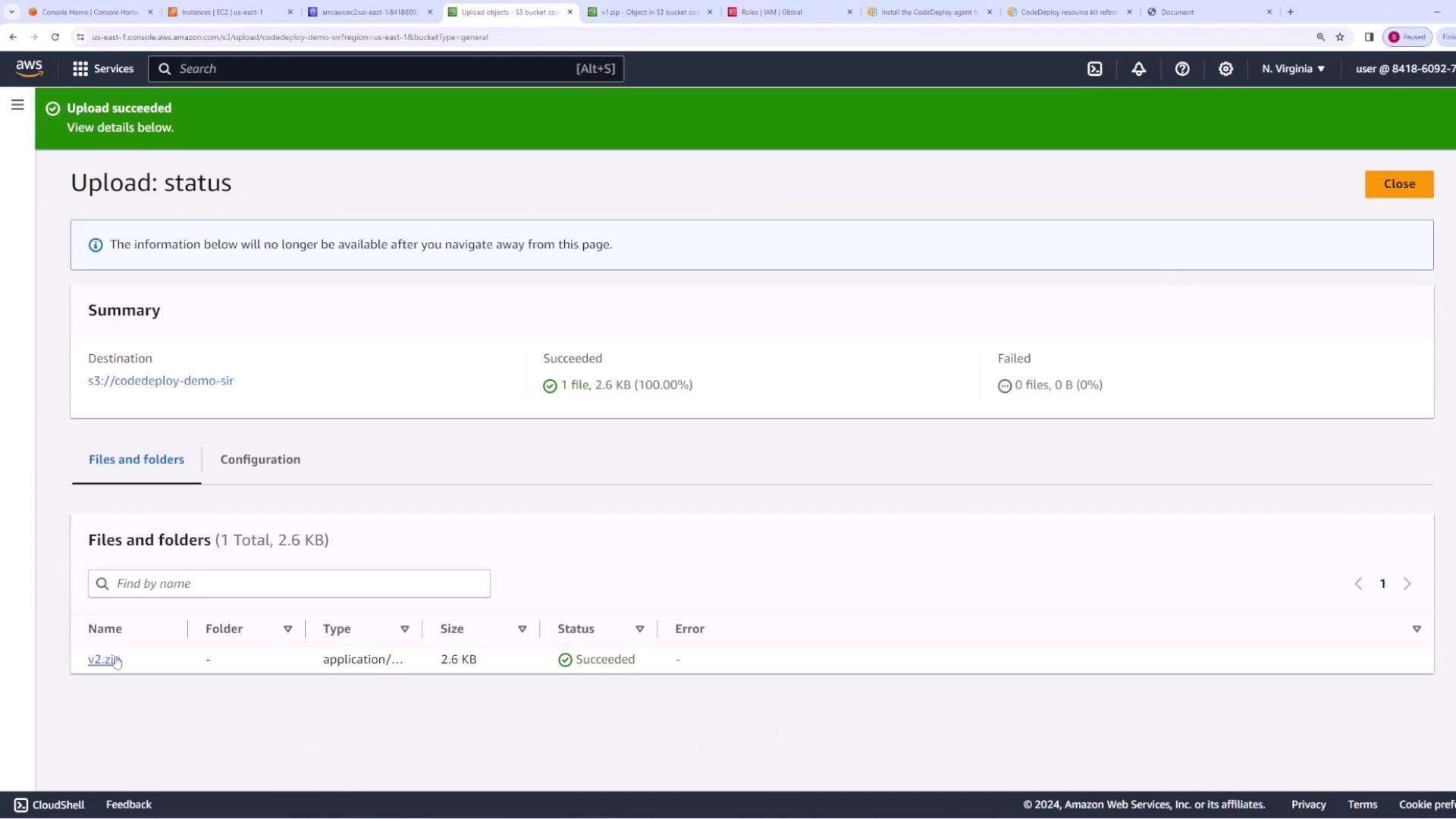 The image shows an AWS S3 upload status page indicating a successful upload of a file named "v2.zip" with a size of 2.6 KB. The summary confirms that 1 file was successfully uploaded with no failures.