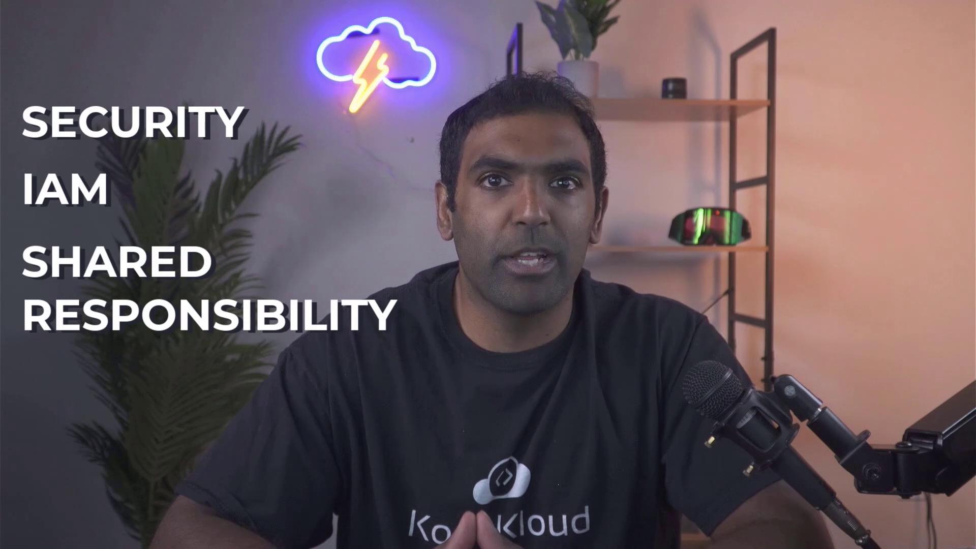 A person is speaking into a microphone with the words "SECURITY," "IAM," and "SHARED RESPONSIBILITY" displayed beside them, under a neon cloud and lightning sign.