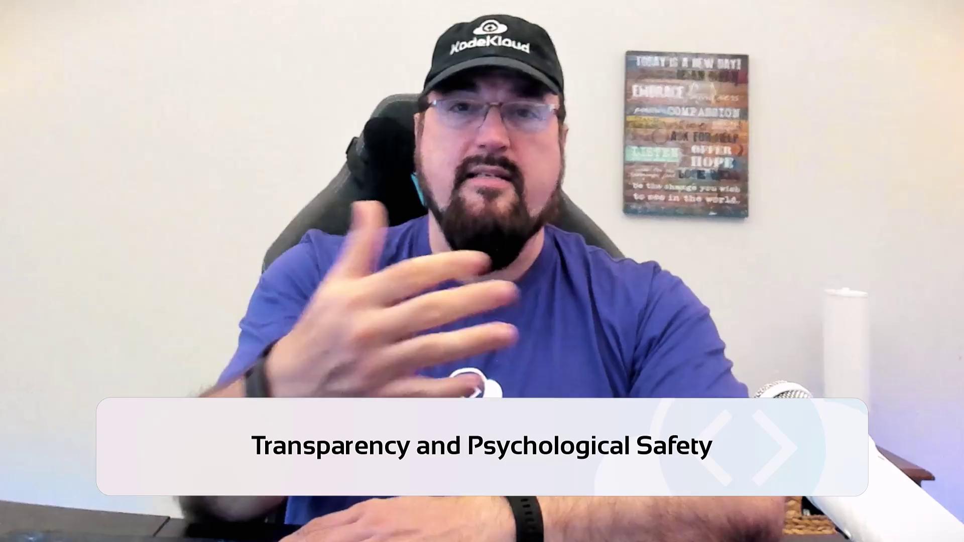 A person wearing a cap and glasses is gesturing while sitting in front of a microphone, with a sign in the background. The text overlay reads "Transparency and Psychological Safety."