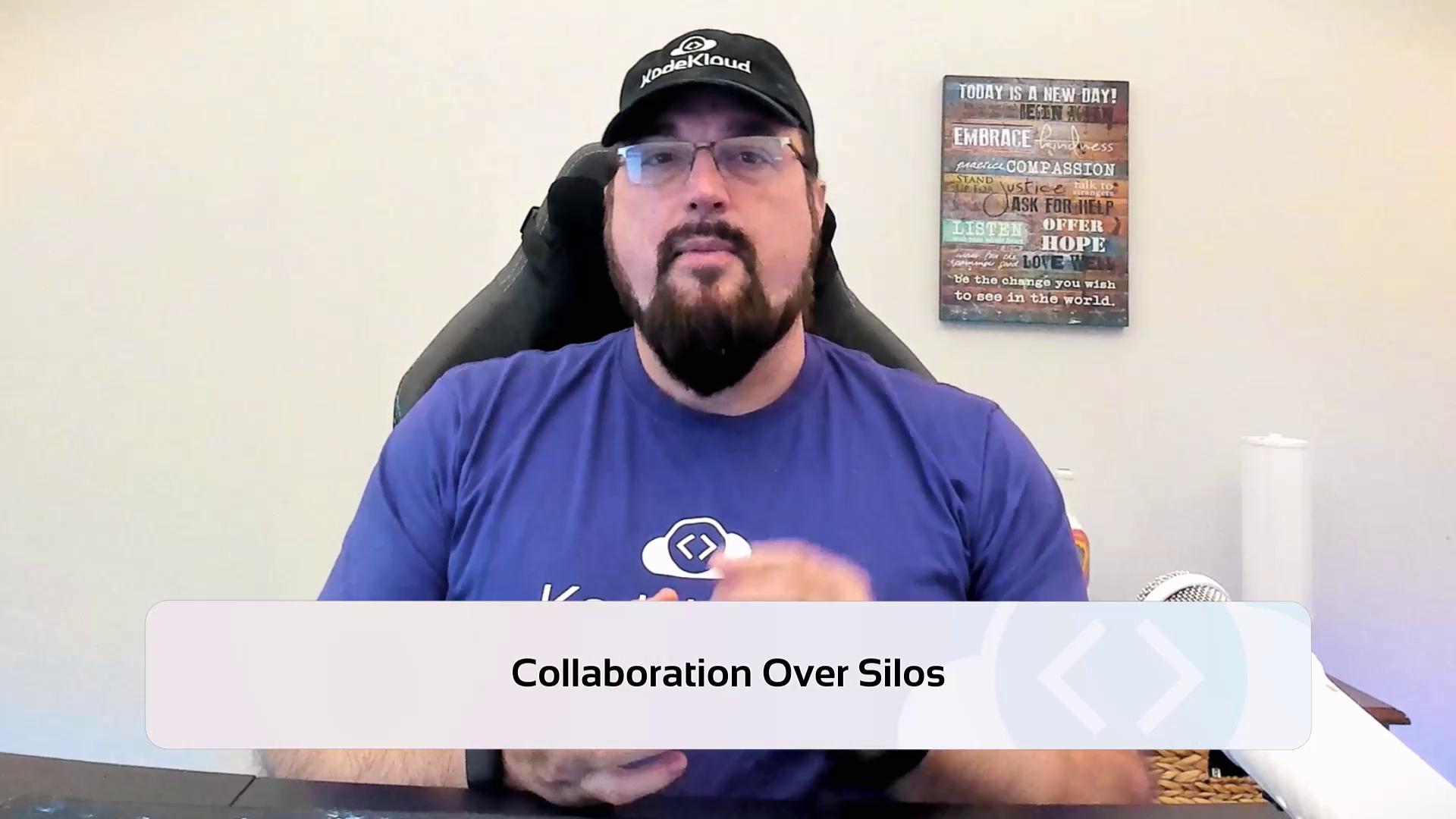 A person wearing a cap and glasses is sitting in front of a wall with a motivational sign, with the text "Collaboration Over Silos" displayed at the bottom.