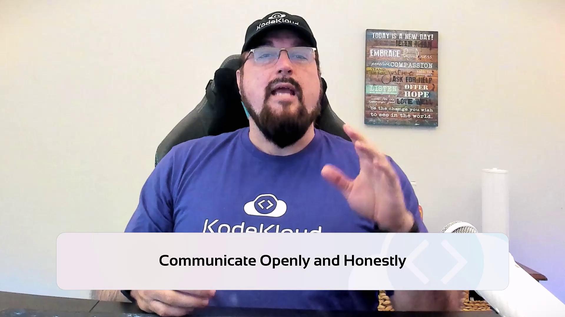 A person wearing a "KodeKloud" shirt and cap is speaking, with a motivational sign on the wall behind them. The text overlay reads "Communicate Openly and Honestly."