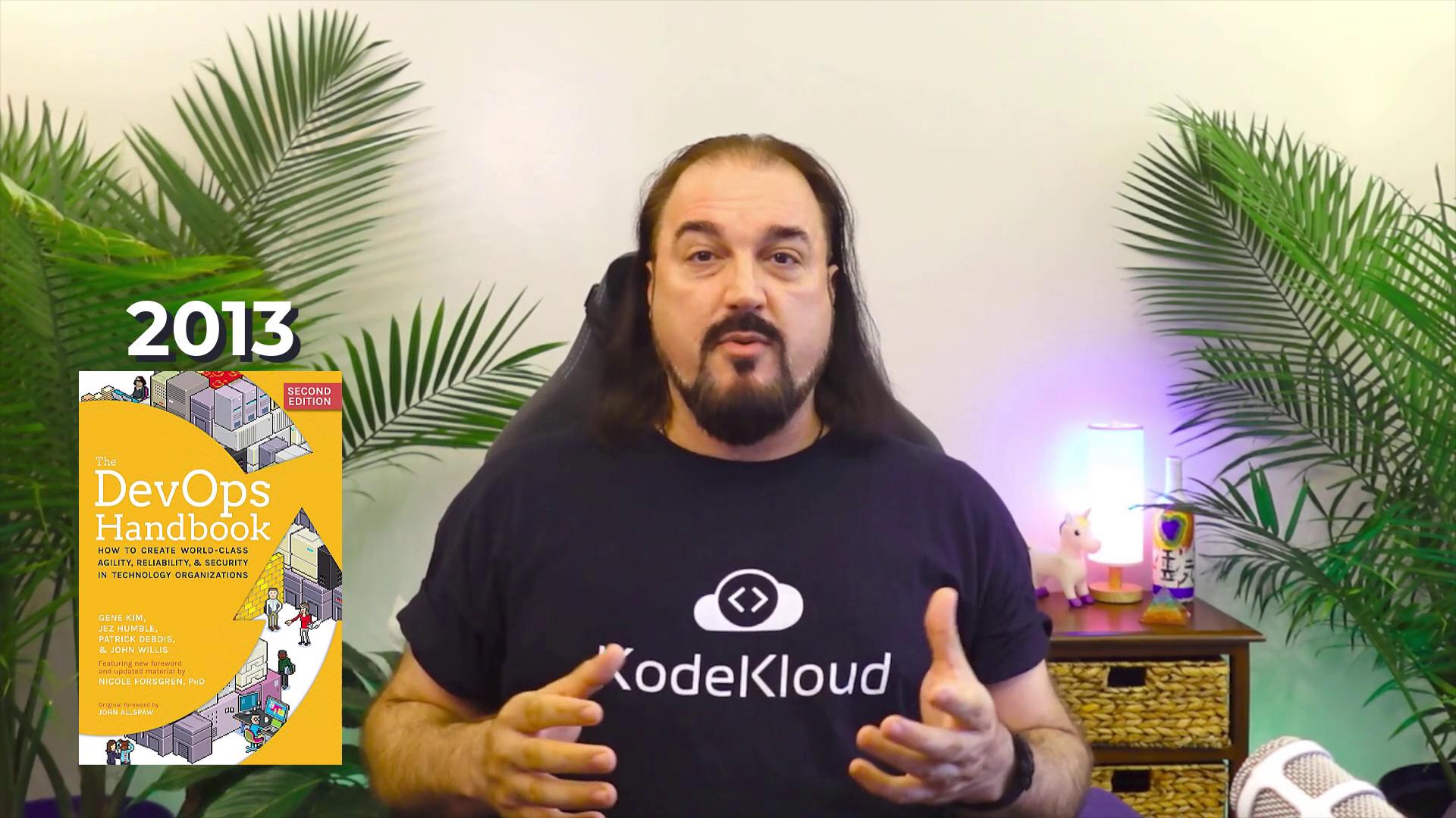 A person in a "KodeKloud" shirt is speaking, with "2013" and "The DevOps Handbook" cover displayed, surrounded by plants and a small lamp.